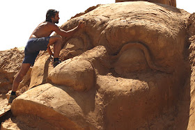 a man works on a sand sculpture of a primate