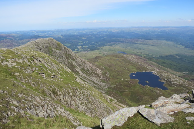 On the left, the rocky north-eastern ridge of Moel Siabod, on the right the lake Llyn-y-Foel. North Wales stretches out to the horizon beyond.