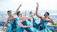 4 dancers of various genders in blue dresses with San Francisco skyline behind them
