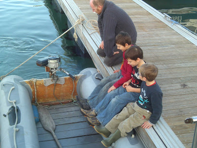 grey dinghy with row of 3 children on pontoon dangling feet into boat