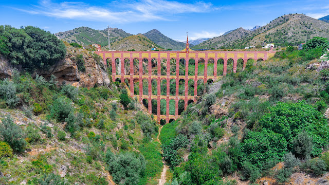 Acueducto de estilo romano sobre un valle y montañas al fondo.