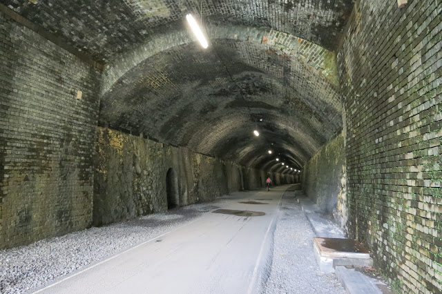 The brick lined tunnel interior with a cycling trail running down the middle and strip lights hanging above.