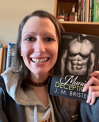 J. M. Brister, holding her book, Manic Deception, in front of a library full of books.