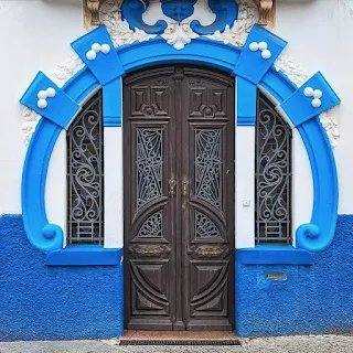 Ornate wooden door in Art Nouveau style on a white facade with bright blue accents