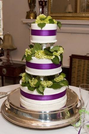 Three tier white wedding cake separated by columns with wide purple satin