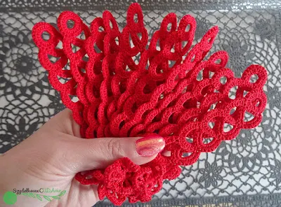 Dwanaście czerwonych zakładek wykonanych szydełkiem ułożonych w dłoni w kształt wachlarzu.