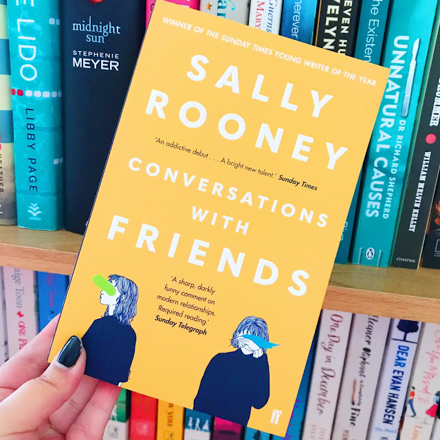 Conversations With Friends by Sally Rooney held up in front of bookshelf