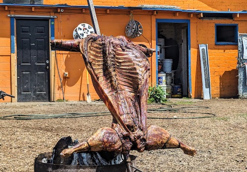 A full cabrito spit-roasting by bright orange Good Choice Tires