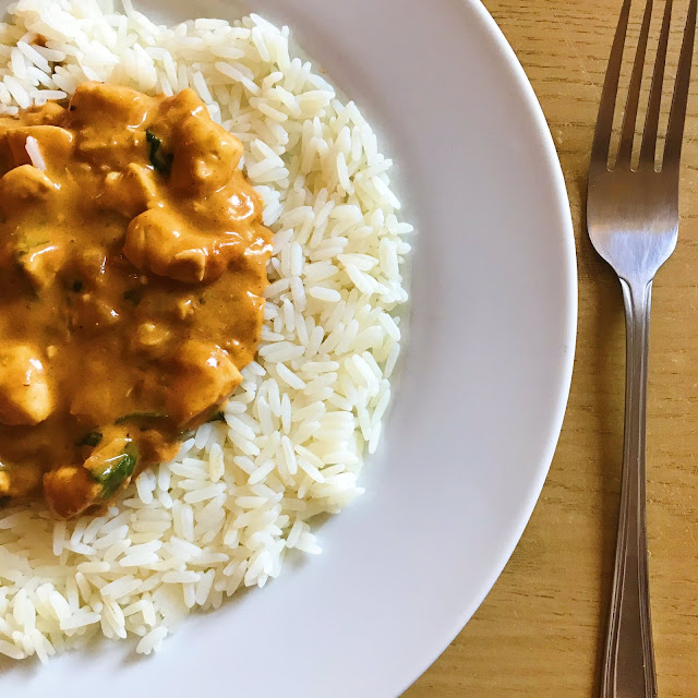 bed of rice on white plate with creamy chicken stroganoff on top. Silver cutlery to the right hand side