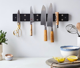 Dark wood knife rack with two magnets in each knife postion. There are three knives, one pair of scissors, and one more item hanging on the rack; three positions are empty so you can see the magnets.