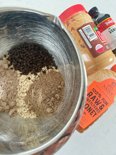 A stainless steel mixing bowl with protein ball ingredients, next to a jar of peanut butter and honey.