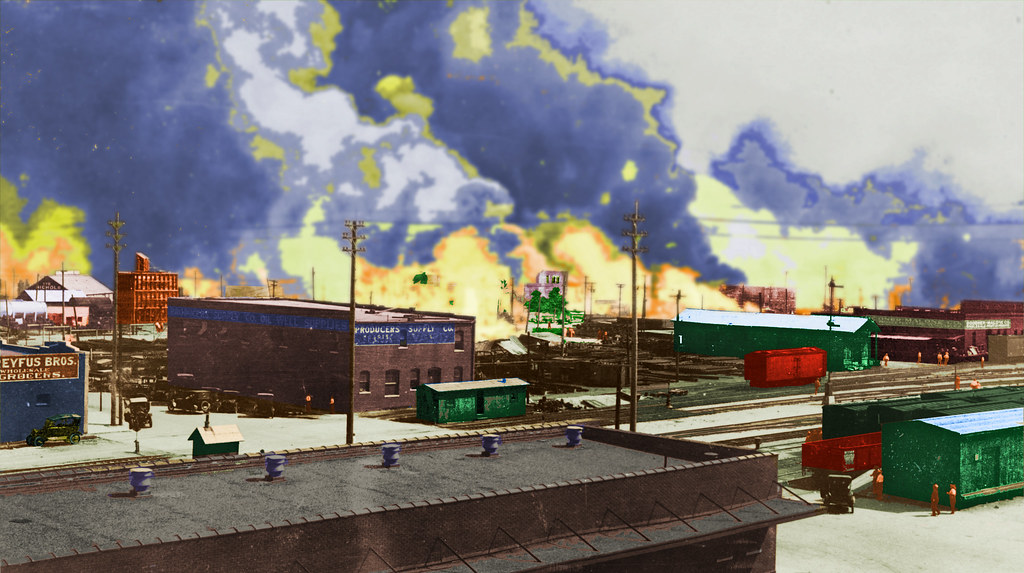 Colorized image from the Tulsa Race Riot. The major fire in the center behind the Producers Supply Company is the Midway Hotel in flames. The building behind it that you can see is the Gurley Building burning. The flames to the right are from the Williams Building. The as yet unburned building behind the building behind the red train car is the Woods building at the corner of Greenwood and Archer. Based on shadows this was taken about 8 in the morning.     Original photographer is unknown.     Original photo is 1989-004-5-28, McFarlin Library. Department of Special Collections and University Archives. The University of Tulsa (cdm15887.contentdm.oclc.org/cdm/singleitem/collection/p15...). Used with permission.