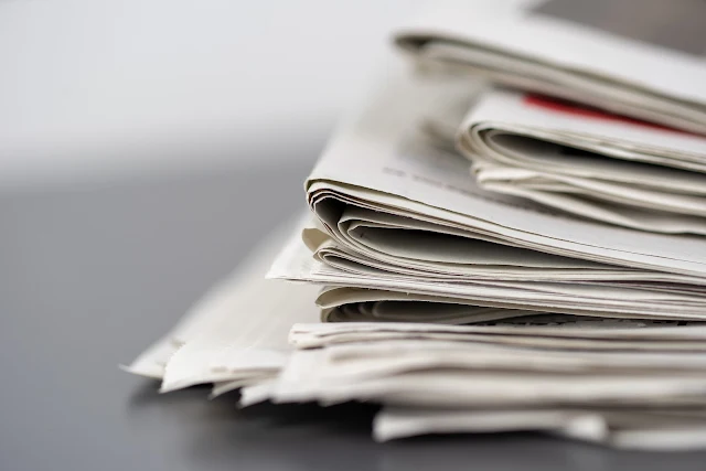 A pile of newspapers containing financial ratios information and news on a grey table