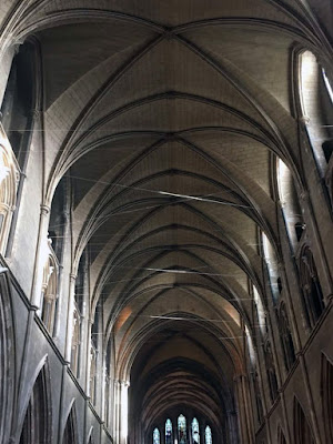 A view of the vaulted ceiling of a white-stone gothic cathedral, with matched galleries of windows and arches on either wall, and a set of five narrow, arched stained-glass windows at the very far end. Strands of monofilament crisscross the vault, catching the light from the windows.