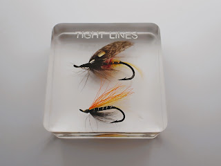 A square resin paperweight containing two fishing flies