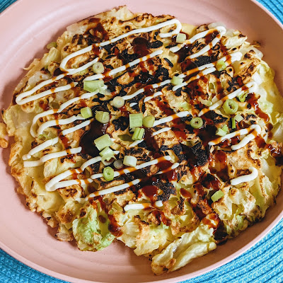 Overhead view of an okonomiyaki drizzled with brown and white sauces.