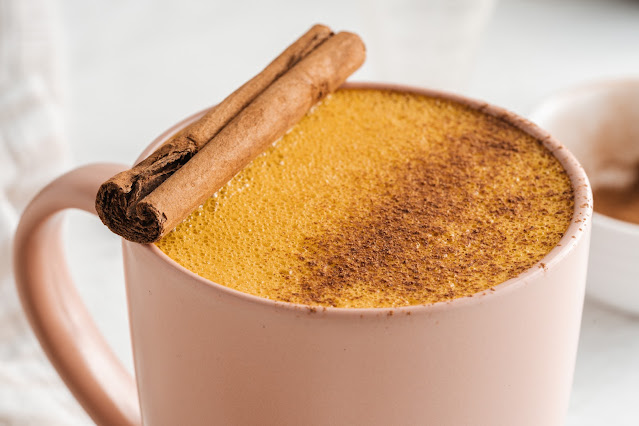latte in pink mug with cinnamon sprinkled on top with cinnamon stick garnish.