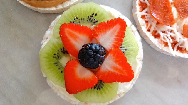 a close up of the fruit pizza rice cake with sliced kiwi, strawberries, and a blackberry in the center