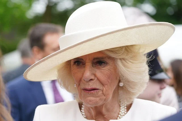 Queen Camilla wore a blue midi dress. The Queen wore an ivory two-tone coat and white midi dress. Coronation Garden in Newtownabbey