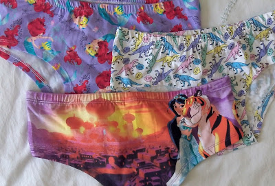 Three pairs of underpants, two with Disney designs on them, one with a dinosaur print, laid out on a bed.