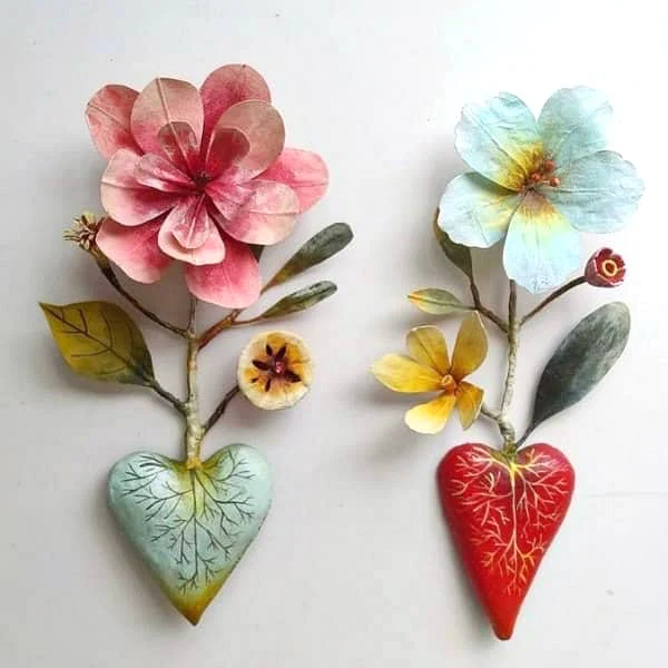 a paper mache flower emerges from each of two painted paper mache hearts