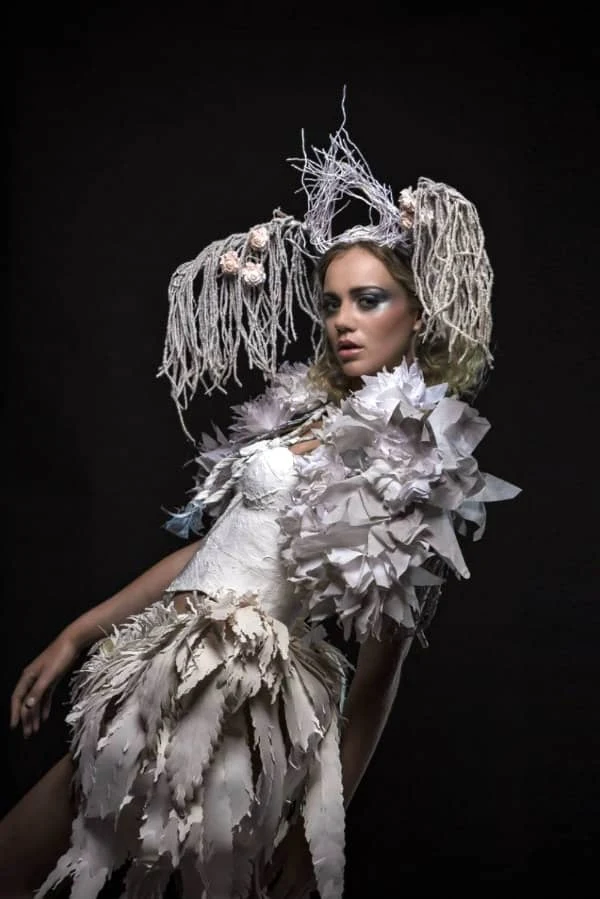 young female model leaning backwards dressed in elaborate silver paper feathered outfit and string-like headpiece