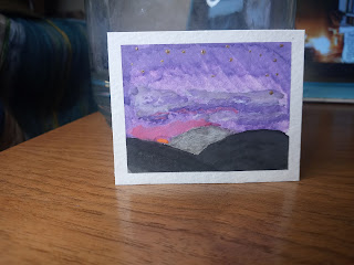 [Image Description] Miniature painting standing up against a large jar of water for brush cleaning. Painting is of gold stars staring to fill a purple sky just as the sun is setting behind shadowy hills.