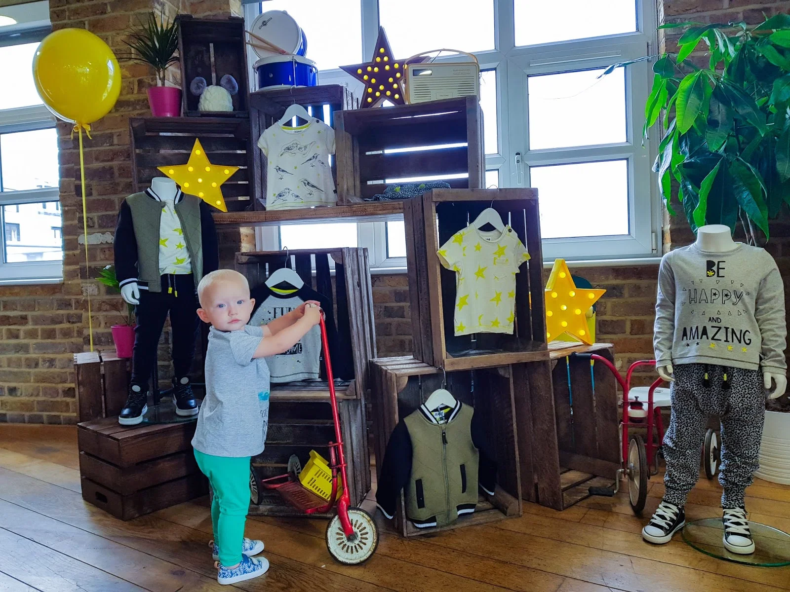 Little standing holding a scooter in front of a display showing boys clothes