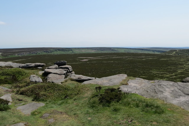 A view across open moorland to Burbage Rocks, a crescent-shaped escarpment with a gap in the middle.