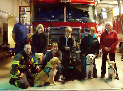 Puppy raisers and their pups posing in front of a fire truck