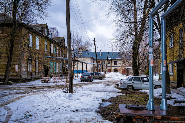 Припаркованные машины в сугробах во дворе деревянного дома