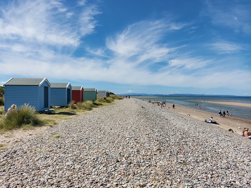 Row of colourful beach huts on a pebbled beach alongside sand and sea