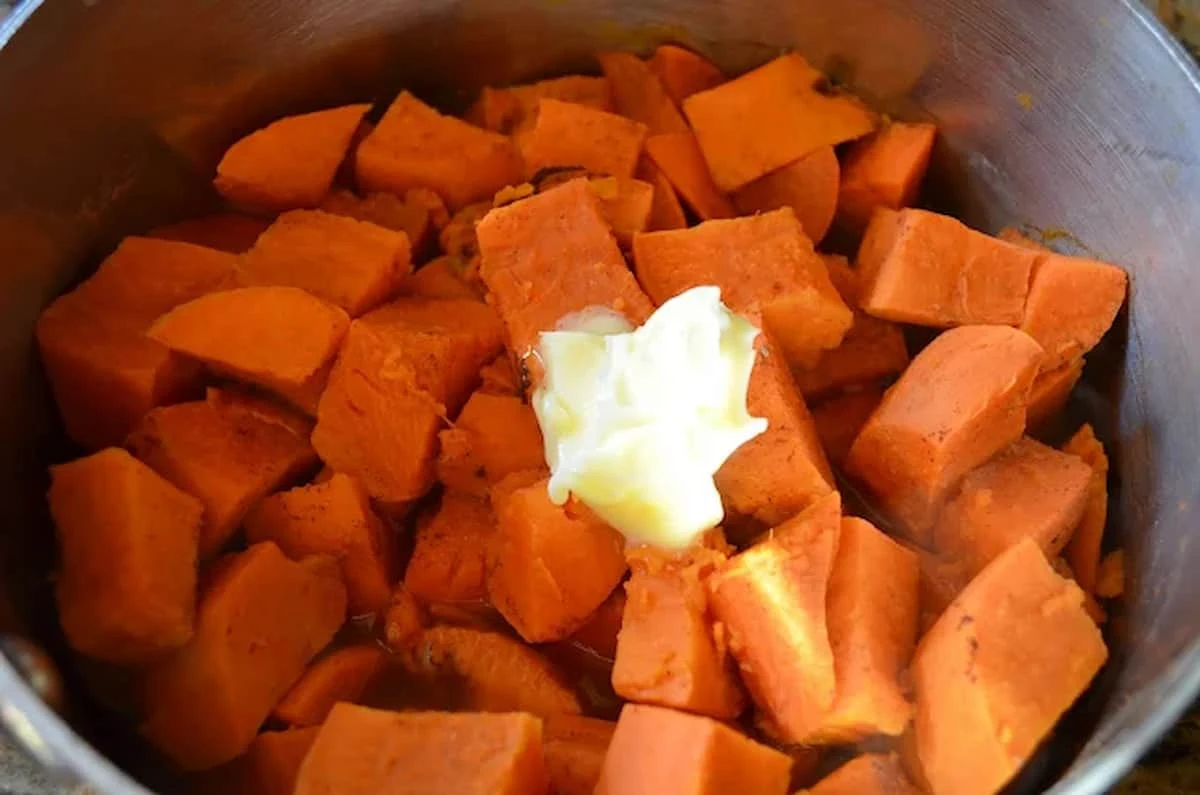A stainless steel pot with diced yams and butter added.