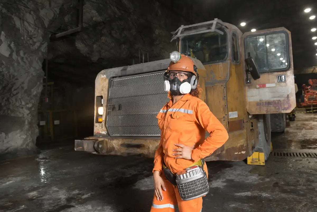 Mulher em frente a maquinario pesado em uma mina subterranea