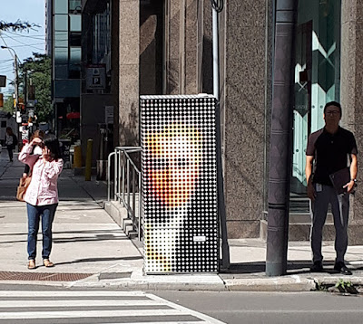 A traffic signal box with a graphic wrap on it, featuring a pixelated portrait