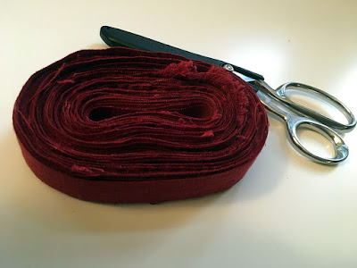 A neatly wound oval disk of narrow red linen strips on a white table, with a large pair of silver sewing shears in their black plastic sheath tucked behind the disk.