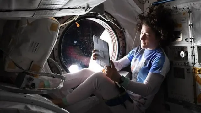 Astronaut reading a letter from home with a UFO right outside of the ISS window.