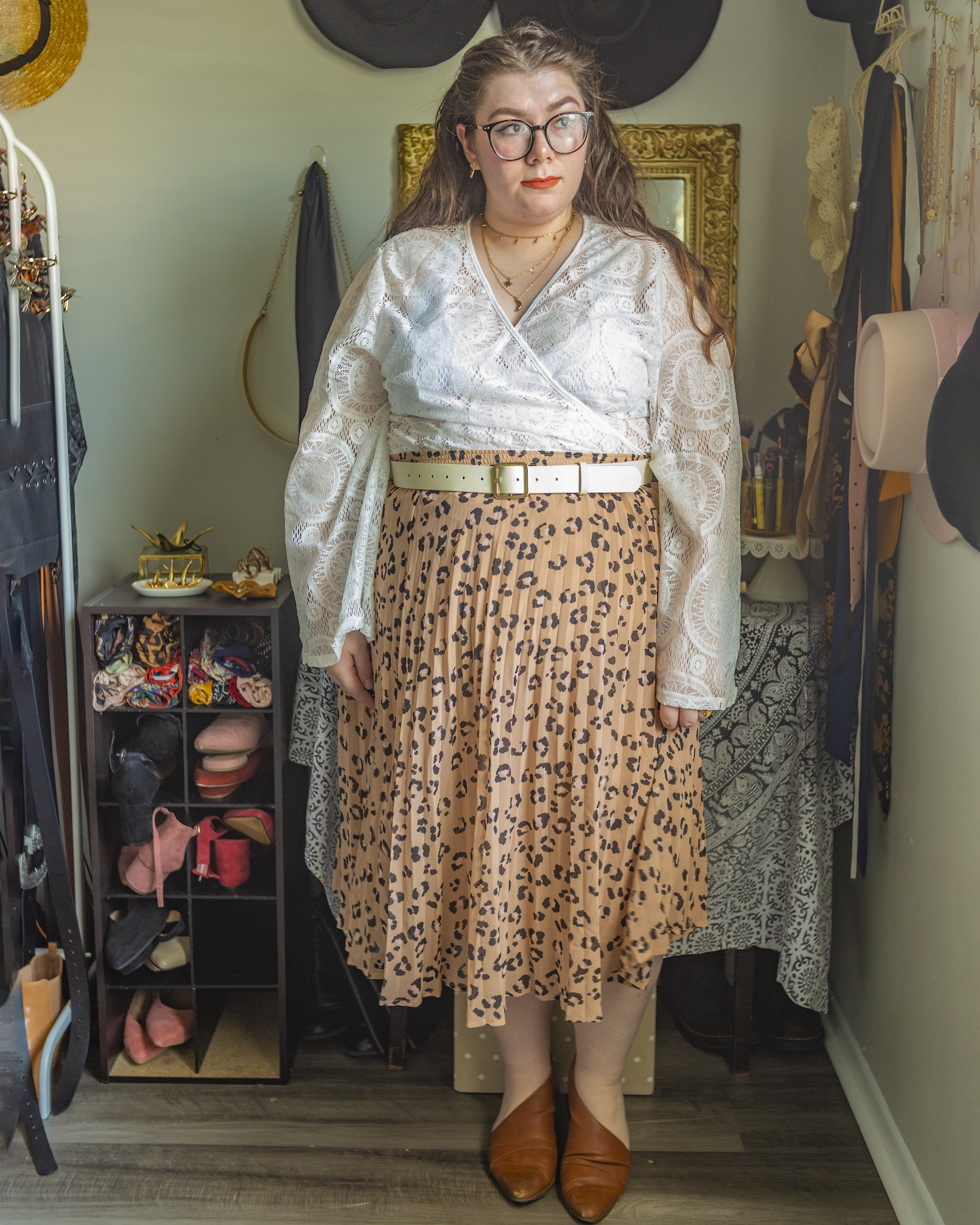 An outfit consisting of a white lace angel sleeve wrap top tucked into a beige leopard print pleated midi skirt and cognac brown d'orsay flats.