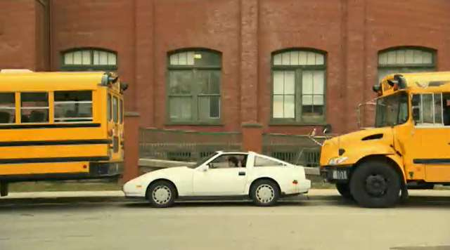 A parked car squeezed between two buses.