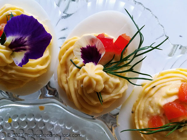 Deviled eggs decorated with pansy and viola edible flowers, dill, red peppers and pickled mustard seeds