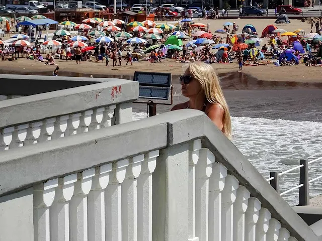 Joven en escalera y de fondo la gente en la playa.