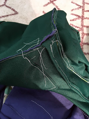 A close-up of the corner of a dark hunter green bag with white stitching and blue lining fabric showing at the seams, and many white thread ends sprawling all over from the ends of the stitching lines.