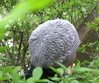 someone wearing a knit hat, worked in fingering-weight grey yarn and leaf lace motif. The ribbed brim is folded up.