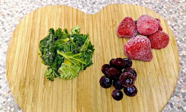 Frozen berries and kale arranged on a wooden chopping board. 