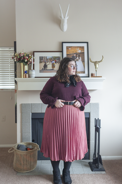 An outfit consisting of a purple sweater tucked into a pink pleated midi length skirt.