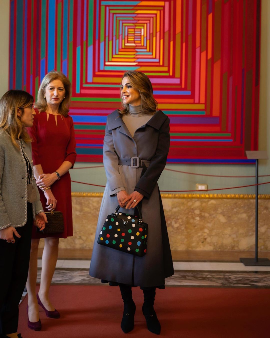 Queen Rania wore a an Ombre shade Fendi off-the-shoulder belted coat with her Salvatore Ferragamo grey turtleneck sweater and a black skirt. She paired the outfit with Jennifer Chamandi Alessandro 105 Black suede long boots and her Louis Vuitton x Yayoi Kusama Capucines Bag