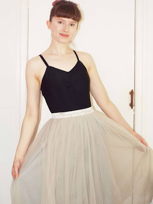 Ellie wearing a large grey tulle skirt, with black leotard and hair up in a bun, with pink bow.