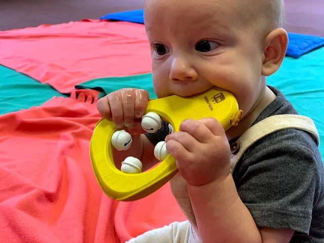 6 month old baby boy eating a bell toy in a music class