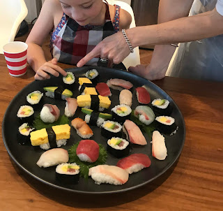 A round platter of both nigiri and nori rolls with hand pointing at them