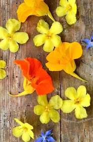 Auf hölzernem Untergrund liegen Blüten in den Farben gelb, orange und blau.